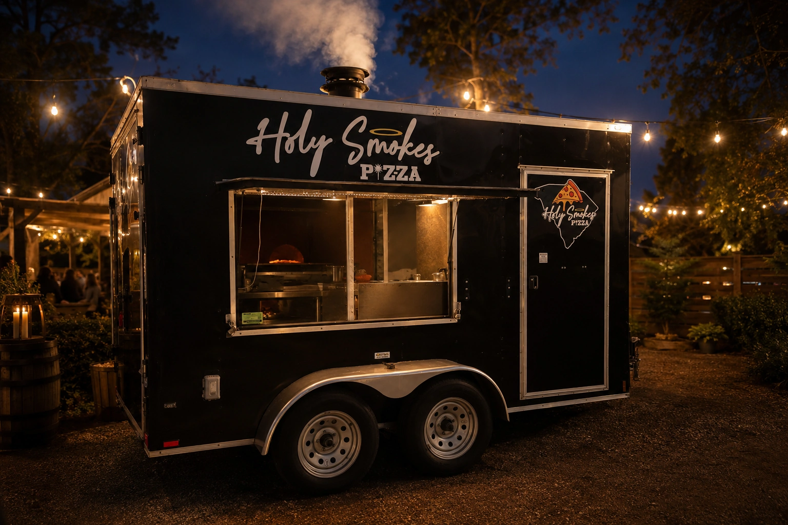 The Holy Smokes Pizza wood-fired trailer glowing under string lights at night