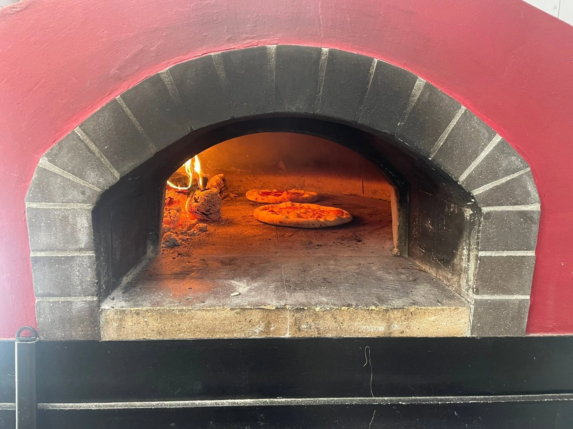Two Neapolitan pies baking inside the red wood-fired oven
