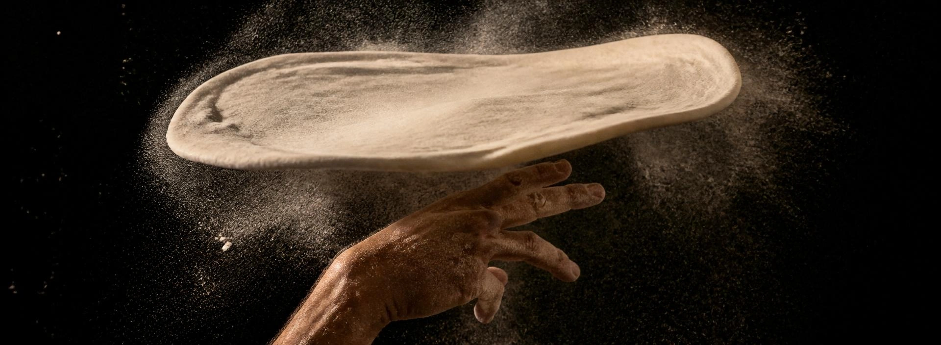 A pizza maker hand-tossing dough into the air