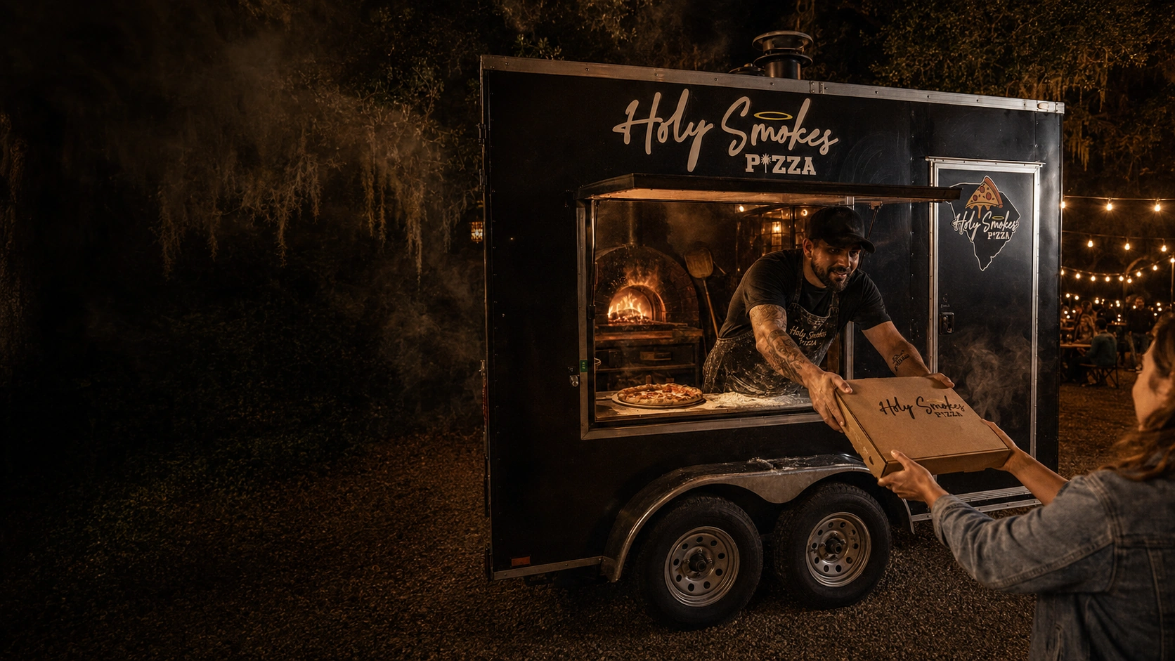 Holy Smokes Pizza trailer serving guests at night under string lights