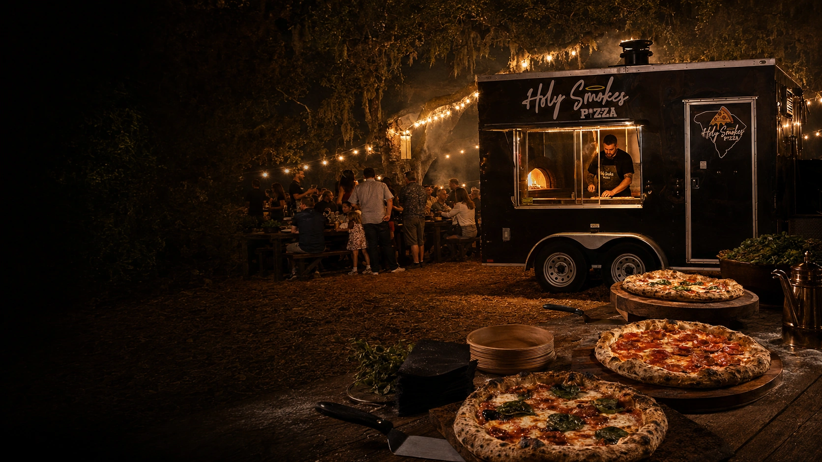 The Holy Smokes Pizza trailer serving guests under string lights at night