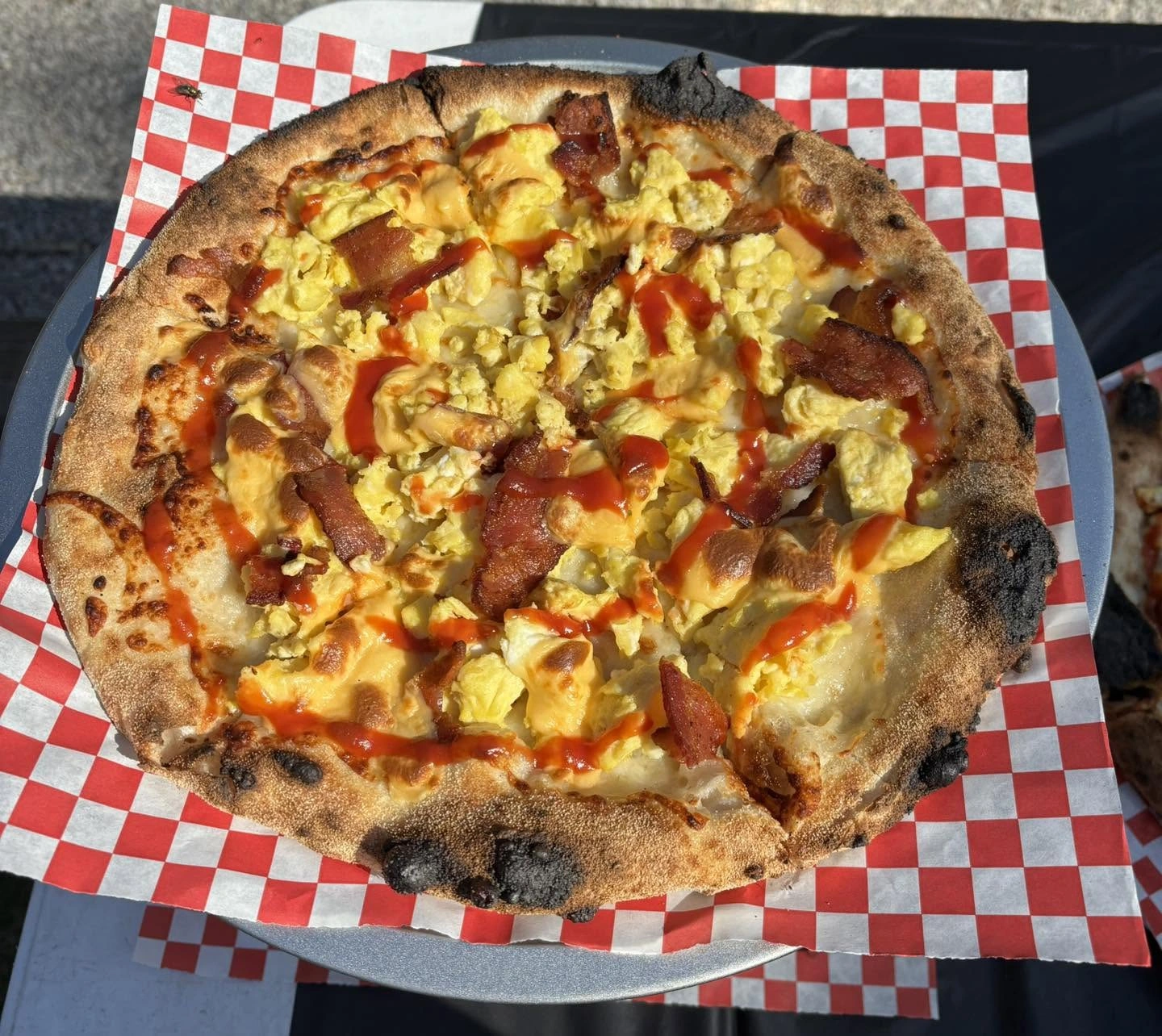A wood-fired breakfast pizza with bacon, egg, and drizzled sauce