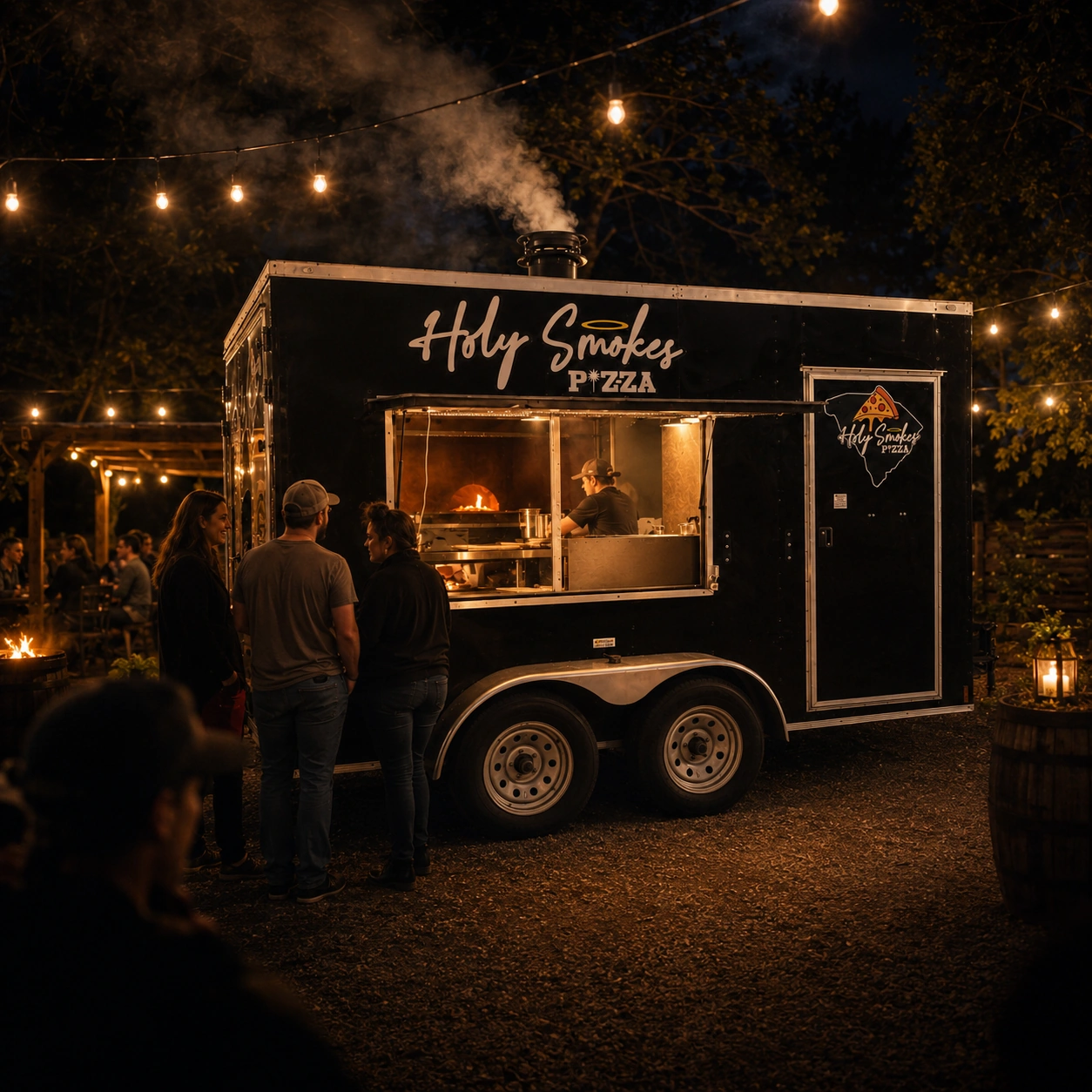 The Holy Smokes Pizza wood-fired trailer serving guests under string lights at night