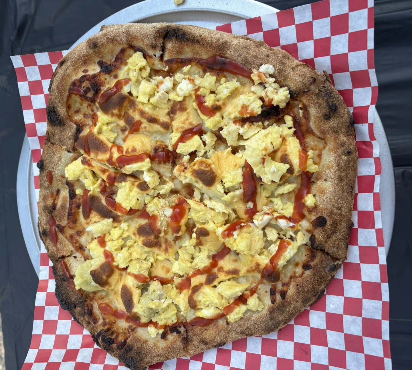 A wood-fired breakfast pizza topped with scrambled eggs and hot sauce